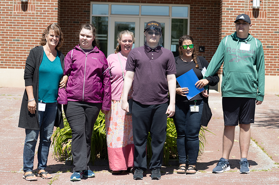 Is-Alfond-Hall A group of six people stands in front of a building. They are dressed casually and smiling. One person holds a blue folder. Saint Joseph's College of Maine